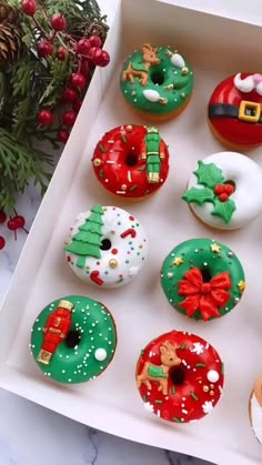 twelve decorated donuts in a white box on a marble table with holly and santa clause decorations