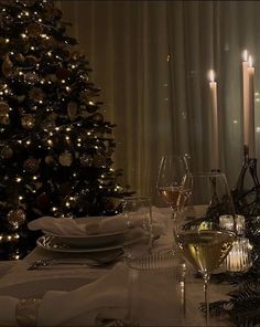 a table set with wine glasses, plates and candles in front of a christmas tree