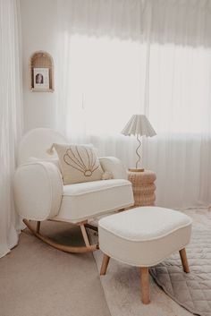 a white rocking chair and foot stool in a living room with curtains on the windowsill