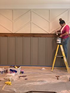 a woman standing on a ladder painting the walls