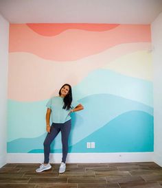 a woman standing in front of a colorful wall with mountains painted on the wall behind her