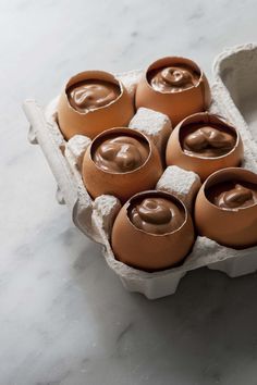 six eggs in an egg carton with chocolate frosting on the top and inside