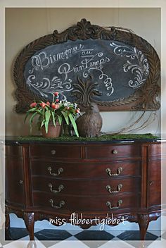 an old dresser has a chalkboard sign above it and flowers on the top shelf