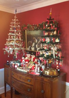 a christmas tree with ornaments on it in front of a red wall and a painting