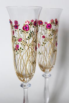 two wine glasses decorated with flowers and gold stemings, one is clear and the other has floral designs on it