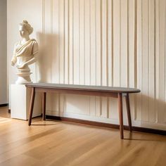 a white marble busturine sitting on top of a wooden bench next to a wall