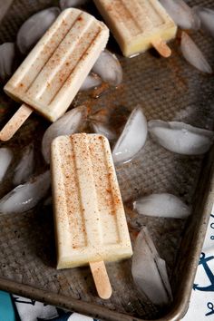 three popsicles sitting on top of ice cubes in a metal pan next to each other