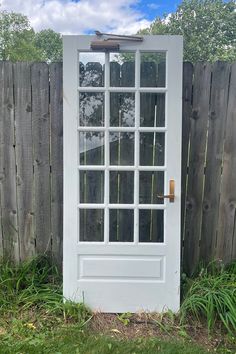 a white door sitting in the grass next to a wooden fence with a sky background