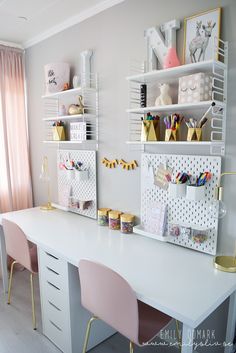 a white desk topped with two pink chairs next to a wall mounted shelf filled with craft supplies