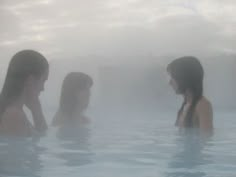 three women are in the water with steam coming out of their backs and behind them