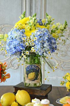 a vase filled with blue and yellow flowers sitting on top of a table next to lemons