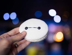 a person is holding up a small white cookie with black dots on the face and eyes