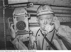 black and white photograph of a man wearing a helmet talking on a cell phone while holding something in his hand