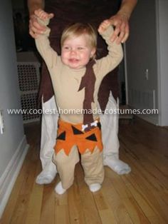 a man holding a child in his arms while standing on the floor wearing an orange and brown costume