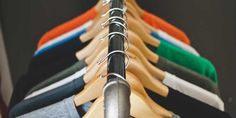 a row of clothes hanging from a metal rack in front of a wall with several different colored shirts on it