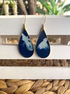 These cyanotype earrings feature photographic prints made from real botanicals, the sun and water! The prints were created by placing botanicals on watercolor paper coated in photo-reactive chemicals then exposed directly to the sun. The result this stunning Prussian Blue background contrasted by the white silhouettes of the botanicals. Every print is one of a kind and there are slight variations from piece to piece.  The cyanotype print was then sealed and placed in an antique gold bezel, and completed with resin. The back of the earrings are covered with a lightweight cork material. These earrings are each a one of a kind piece of art! This design features a teardrop shape measuring 2 1/2 inches. The earring hooks are stainless steel. All of my pieces of jewelry were created from a place Cyanotype Earrings, Cyanotype Print, Alternative Photography, Cork Material, Prussian Blue, Earring Hooks, Unique Earrings, My Flower, Flower Earrings