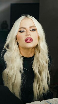 a woman with long blonde hair and pink lipstick on her lips looking at the camera