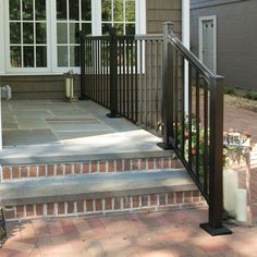 a front porch with brick steps and black iron handrails, surrounded by flowers