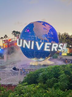 the universal sign is lit up and surrounded by greenery in front of an amusement park