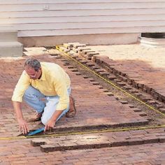 a man kneeling down next to some bricks and measuring the area for laying tiles on it