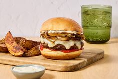 a hamburger and some potato wedges on a cutting board next to a green drink