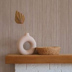 a white vase sitting on top of a wooden shelf next to a basket and wallpaper