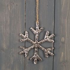 a snowflake ornament hanging from a rope on a wooden wall with wood planks