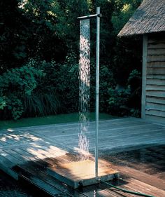 a water fountain on a wooden deck in the middle of a garden with trees behind it