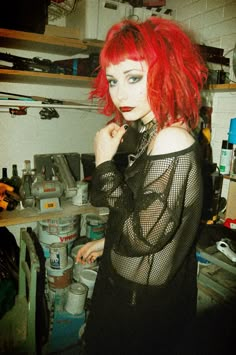 a woman with red hair and blue eyes in a room full of cluttered items