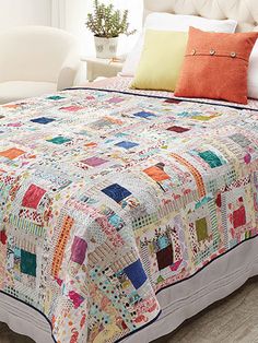 a bed with a colorful quilt on top of it next to a white chair and potted plant