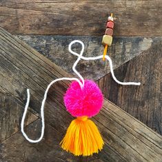 an orange and pink pom - pom hanging from a string on a wooden surface