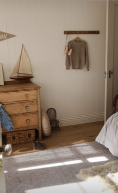 a bed room with a neatly made bed next to a wooden dresser and hanging clothes