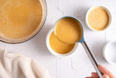 a person is holding a spoon over some liquid in small bowls on a white table