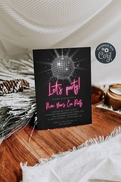 a black and pink party card on top of a wooden table next to pine cones