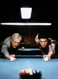 two men leaning over a pool table to look at the billiards ball in front of them