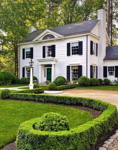 a large white house with black shutters and green grass in the front yard area