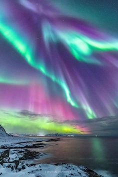 the aurora bore is glowing brightly in the night sky over water and snow covered mountains