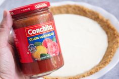 a hand holding a jar of confectia on top of a white plate next to a pie crust