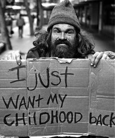 a man holding a cardboard sign that says i just want my childhood back