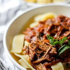 a bowl filled with pasta and meat on top of a white table cloth next to a fork