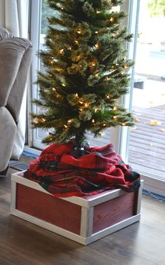 a small christmas tree in a wooden box on the floor next to a couch and window