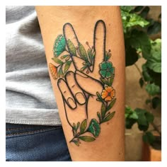 a person with a tattoo on their arm holding up the peace sign in front of flowers