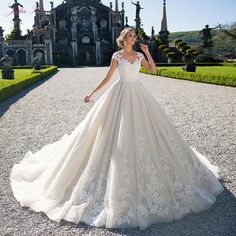 a woman in a white wedding dress standing on a gravel road with an old castle in the background