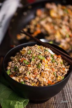 a black bowl filled with rice and vegetables next to chopsticks on a table