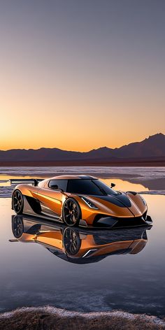 an orange sports car sitting on top of a body of water at sunset with mountains in the background