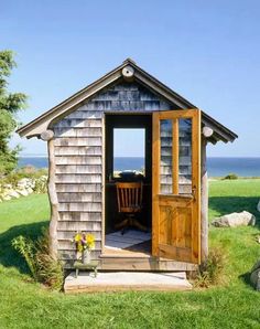 a small wooden shed sitting on top of a lush green field next to the ocean