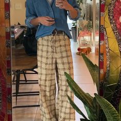 a woman taking a selfie in front of a mirror with her cell phone and potted plant