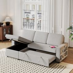 a living room with a gray couch and an open storage compartment on the floor in front of a window