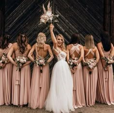 a group of women standing next to each other in front of a wooden wall holding bouquets