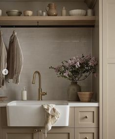 a white sink sitting under a window next to a wooden shelf with dishes on it